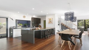 Eine moderne Küche mit einer zentralen Kochinsel, einem Essbereich mit Holztisch und schwarzen Stühlen sowie einer Treppe, die in eine obere Ebene führt.