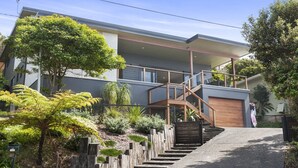 Ein modernes Haus mit zwei Etagen und einer hölzernen Freitreppe, die zu einem Balkon führt.