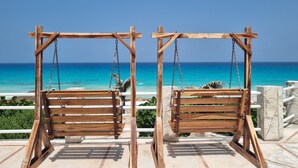 Two wooden swings with chains, positioned on a terrace with a view of the ocean. - Cancun Studio Front Beach (Cancún)
