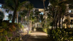 A pathway flanked by lush greenery and palm trees leading to a building with multiple balconies. - Cancun Studio Front Beach (Cancún)
