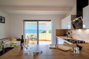 Una cocina moderna con una gran mesa de madera, vista al mar a través de una puerta corrediza de vidrio y un comedor con mesa y sillas.