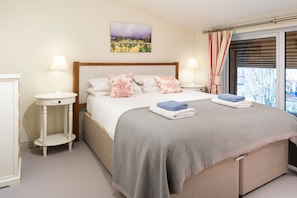 A bedroom with a bed, two bedside tables, a window with curtains, and a painting on the wall. - Sleeps 8, 4 Bedrooms, Dogs Welcome, No Smoking, Wood burner, Wi-Fi*, Garden, Games Room (Cheltenham)
