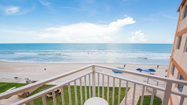 Un balcon avec vue sur la plage, une petite table et un espace herbeux.
