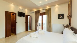 A hotel room with a large bed, a TV mounted on the wall, and a balcony with curtains. - Dimitrios Villa, a Luxury Oasis with Pool & Gym (Rethymno)