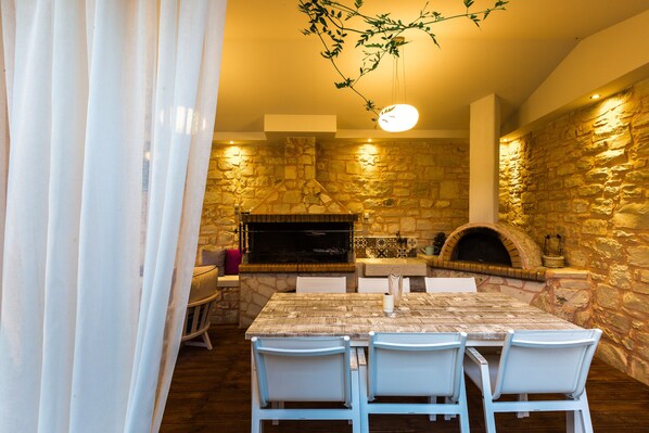 Une cuisine aux murs de pierre, dotée d’un four à pizza, d’une table à manger avec des chaises et d’un luminaire suspendu.