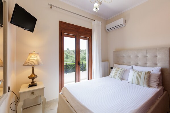 A bedroom with a bed, bedside lamp, air conditioning unit, and a television on the wall.