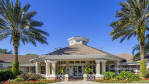 A two-story building with a central entrance, surrounded by palm trees and a garden with red flowers. - Treasure Hunt by VillaDirect (Kissimmee)