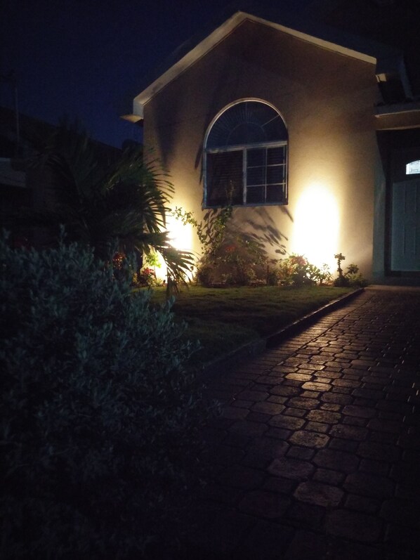 Une maison avec une allée pavée menant à un garage, entourée de verdure et éclairée par des lampes extérieures.