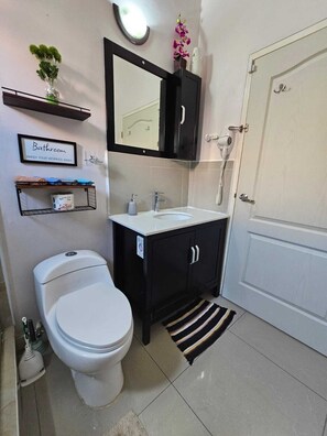 A bathroom with a toilet, sink, and mirror. There is a shelf with toiletries and a sign that says "Bathroom." - The Royal Villa by Caymanas Country Club Estate (Caymanas Country Club)