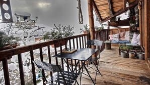 Una terraza de madera con una mesa y sillas, un área de descanso con cojines y plantas en macetas.