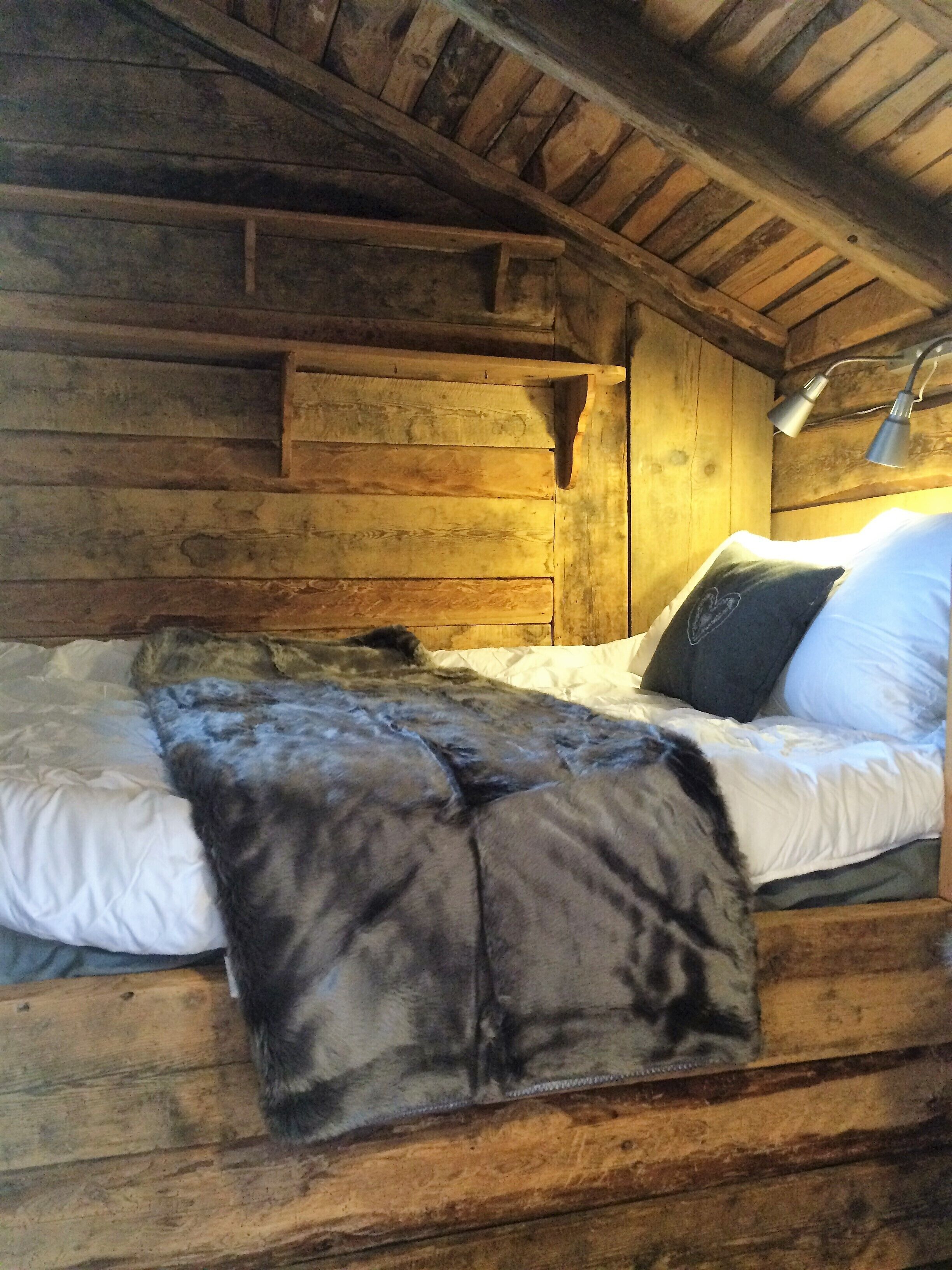 Ein holzgetäfeltes Zimmer im Chalet-Stil mit Bett, Lampe und Fenster.