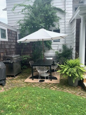 Un patio trasero con mesa y sillas, una parrilla y una planta en maceta.