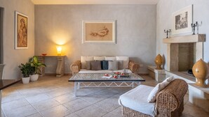 Ein gemütliches Wohnzimmer mit Sofa, Couchtisch und Kamin. Zimmerpflanzen und gerahmte Kunstwerke schmücken die Wände.