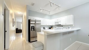 A modern kitchen with white cabinets, a stainless steel refrigerator, a microwave, and a large island with a sink.