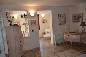 A room with a wooden dresser, a bed with a white headboard, a radiator, and wall-mounted artwork.
