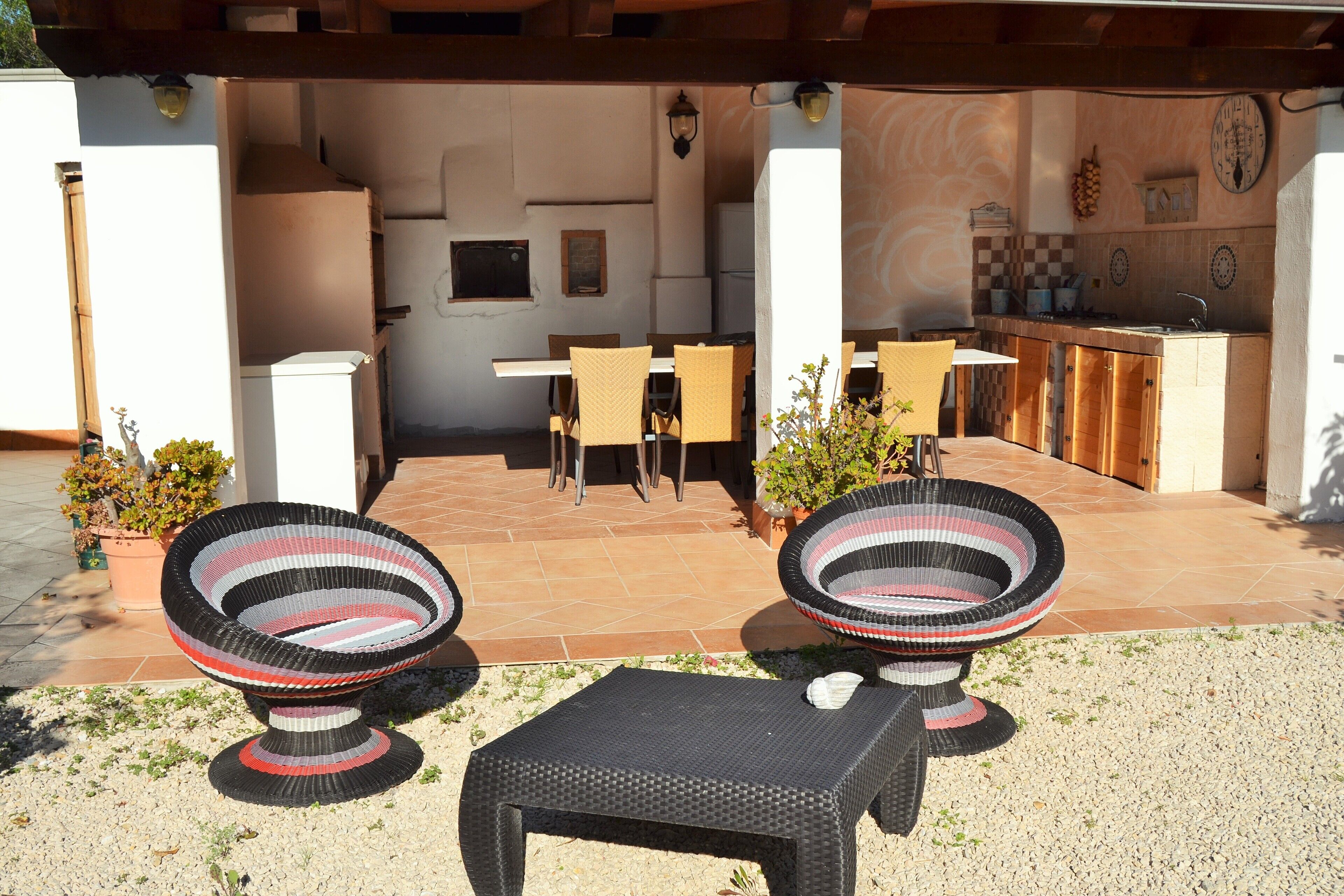 An outdoor patio with wicker furniture, a dining table, and a kitchen area.