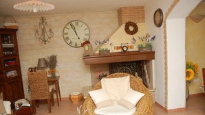 Un salon chaleureux avec un fauteuil en osier, une cheminée et une horloge au mur.