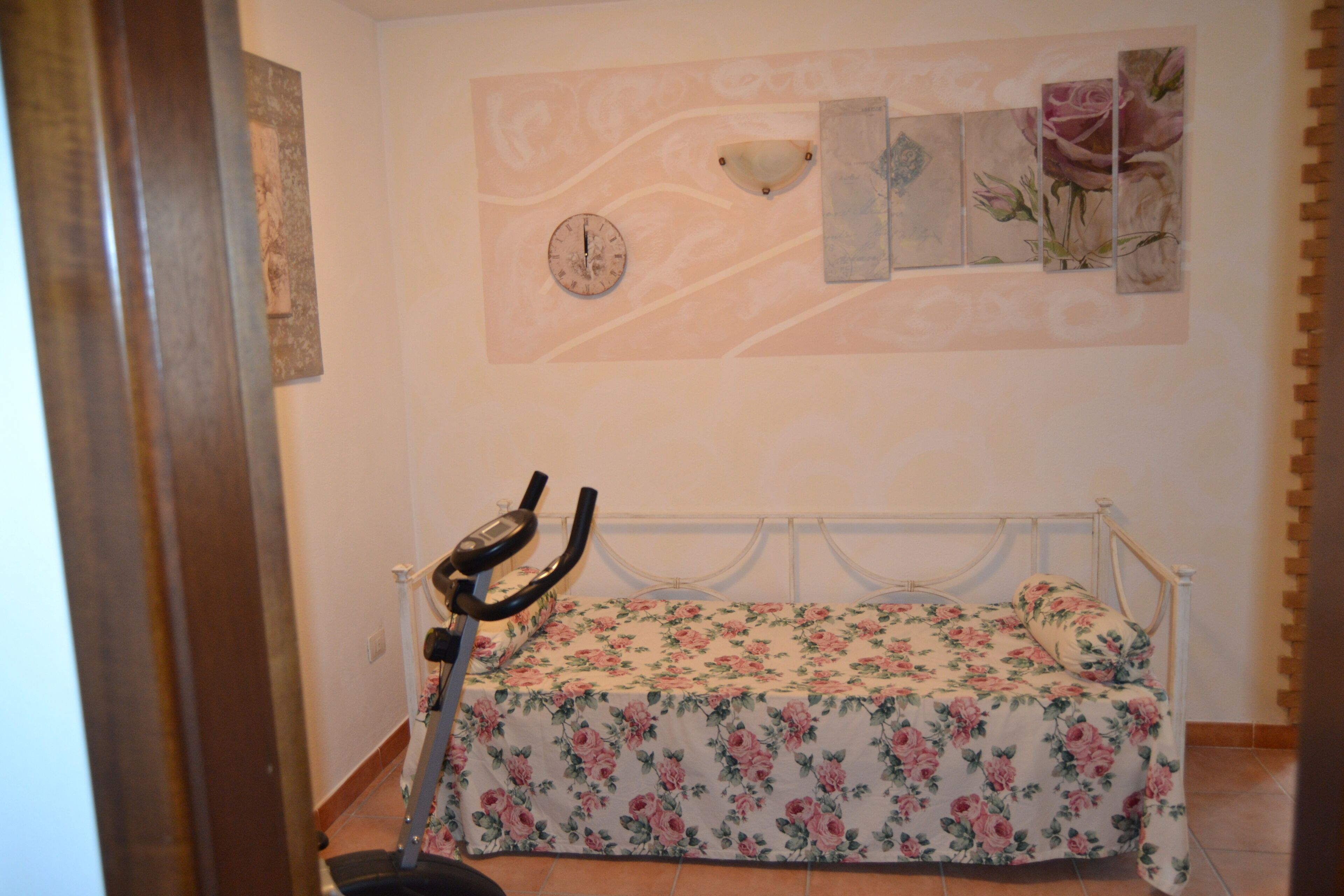 Una camera da letto con un letto, una sveglia a parete e una cyclette stazionaria.