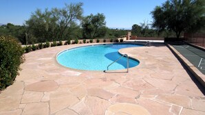 A swimming pool with a stone patio, surrounded by trees and a clear sky. - Foothills Ranch House in Casas Adobes, 8 ac estate with Pool, Tennis, Pickleball (Tucson)