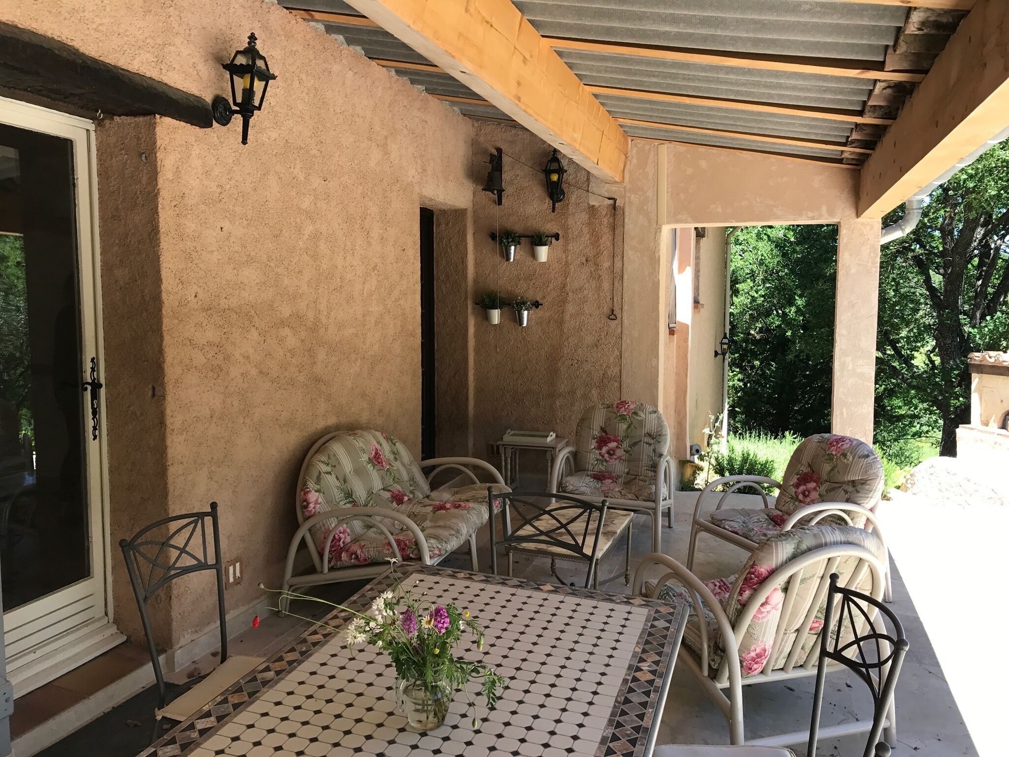 Een buitenpatio met een overdekte zithoek, inclusief een tafel en stoelen, en een potplant.