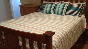 Un lit avec une couvre-lit à rayures et des coussins assortis, une tête de lit en bois et une table de chevet avec une lampe.