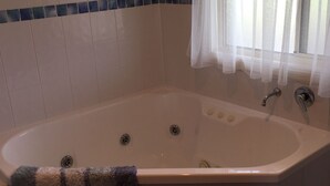 Une salle de bain avec une baignoire beige, une douche et une fenêtre ornée d’un rideau léger.