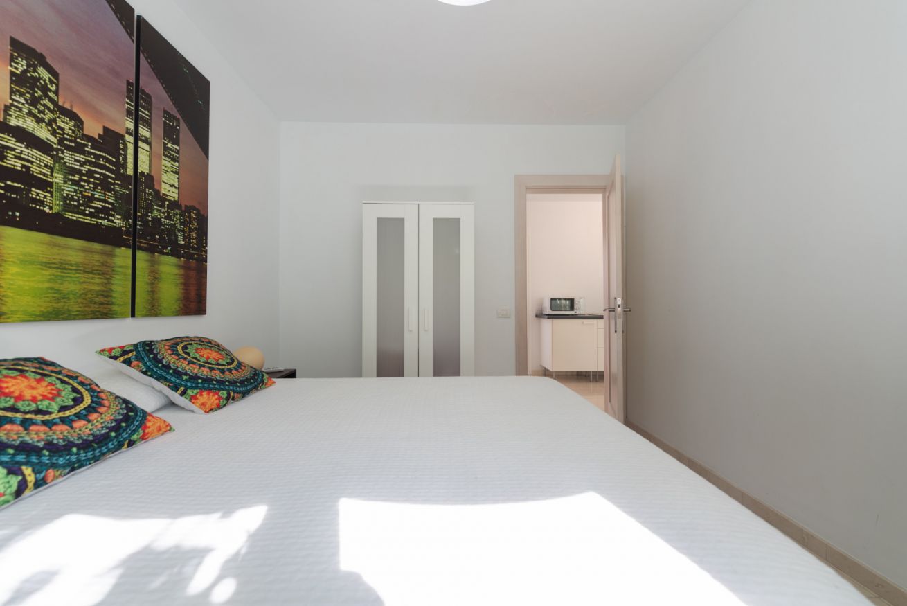 A bedroom with a bed, two pillows, a nightstand, a door, and a view of a cityscape.