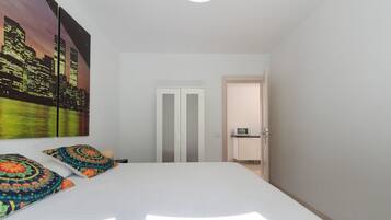 A bedroom with a bed, two pillows, a nightstand, a door, and a view of a cityscape.