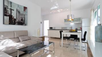 A modern living room with a glass coffee table, a sofa, and a dining area with a white table and chairs.