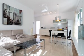 Una sala de estar moderna con una mesa de centro de vidrio, un sofá y un comedor con una mesa y sillas blancas.