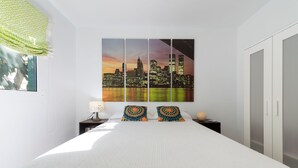 Un dormitorio moderno con una cama grande, una pintura de paisaje urbano, una mesita de noche y un armario.