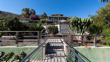 A pathway leading to a building with a staircase, surrounded by greenery and cacti.