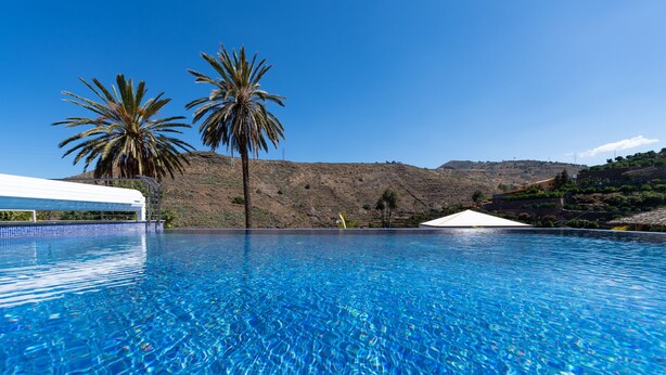 Una piscina azul cristalina con palmeras y un paisaje montañoso al fondo.