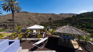 Un resort con zona de piscina, sillas de descanso, una cabaña con techo de paja y vistas a un paisaje montañoso.