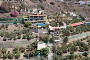 A residential area with a large building featuring a swimming pool, surrounded by greenery and hills.