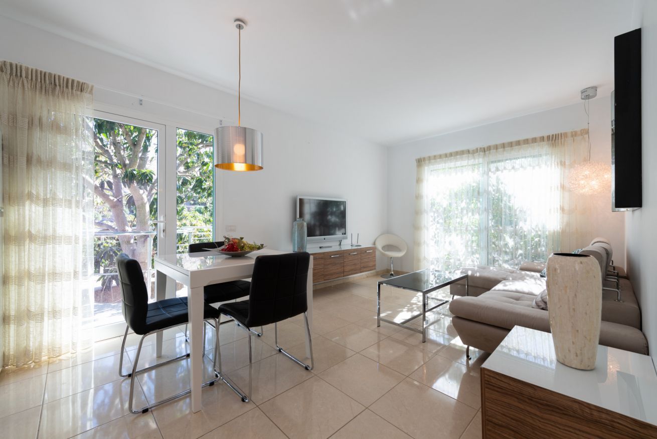 A modern living room with a dining area, a sofa, a TV, and a large window with curtains.