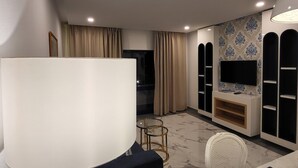 Un soggiorno moderno con una grande lampada bianca, una TV montata su una parete decorata e un'area pranzo con un tavolo e sedie bianche.