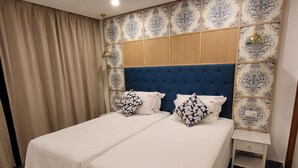 Un letto matrimoniale con biancheria bianca e cuscini a motivi floreali, una testiera in legno e un comodino con una lampada.