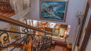 Un magnifique escalier orné de rampes en métal ouvragé, un lustre et un tableau représentant une sirène.