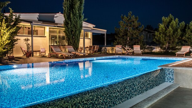 En swimmingpool med solstolar och ett hus i bakgrunden.