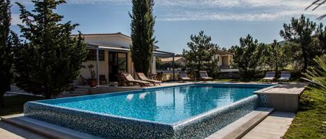 A rectangular swimming pool with a tiled edge, surrounded by a tiled deck and grass.
