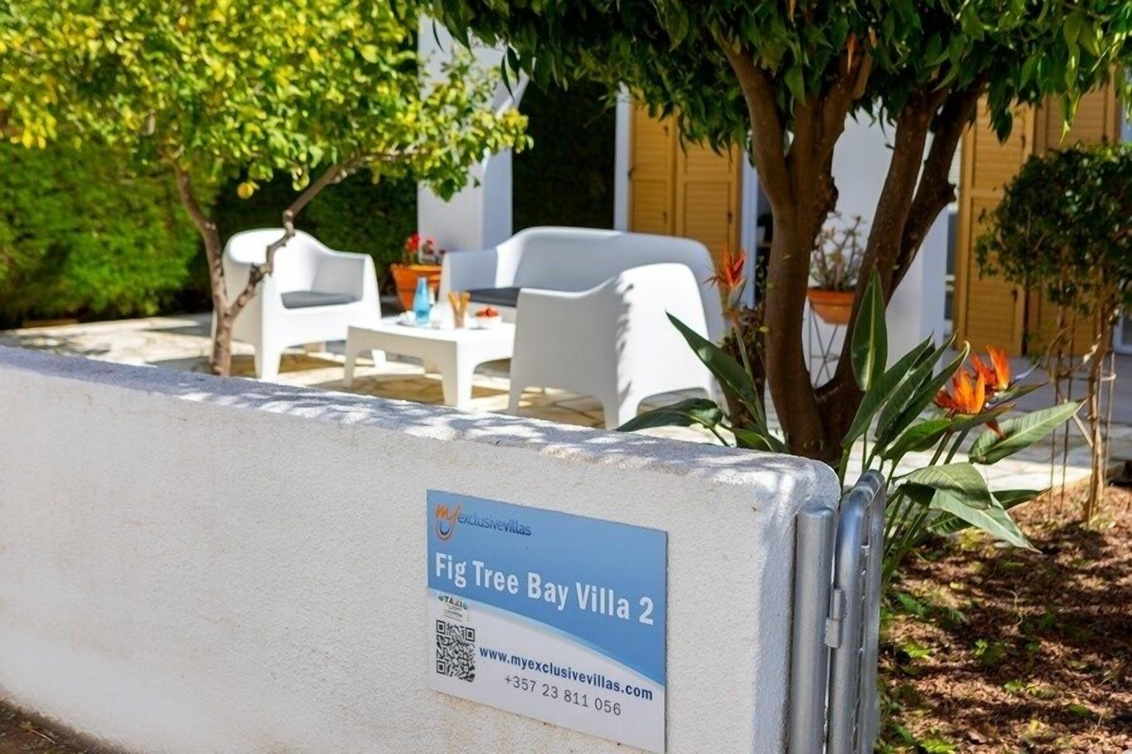 A sign for Fig Tree Bay Villa 2, indicating a property with outdoor seating and a view of the surrounding greenery.