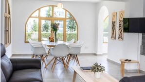 A modern living room with a dining area, large windows, and a flat-screen TV. - This amazing 3 Bedroom villa is located in the center of protaras (Protaras)