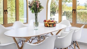 A dining area with a white table and chairs, a vase with flowers, and a fruit basket. - This amazing 3 Bedroom villa is located in the center of protaras (Protaras)