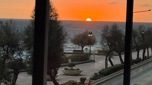 Zonsondergang zicht vanuit een raam, met uitzicht op een straat met bomen en een bankje.
