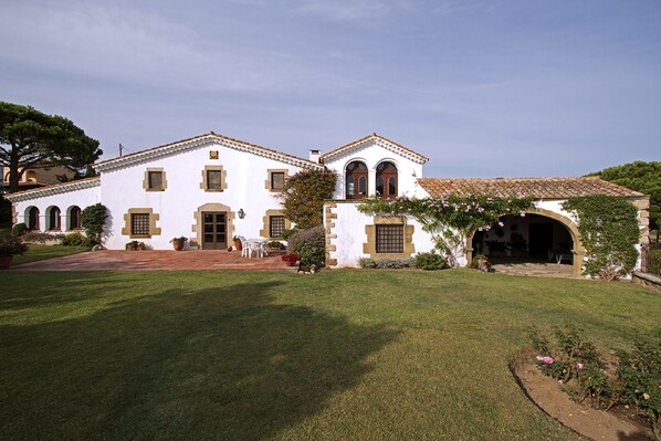 A white building with a tiled roof, arched windows, and a covered entrance. - Rustic farmhouse with sea views, large garden and private pool. (Platja d'Aro)
