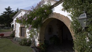Um edifício tradicional com uma entrada em arco, fachada branca e um jardim com plantas floridas.