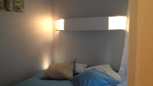 A small, single-bed room with a headboard, two wall-mounted lights, and a blue bedspread. -  BEAUTIFUL 2-ROOM APARTMENT "DESIGN" calm GROUND FLOOR LE LOGIS LE COL D'ASPIN (Lourdes)