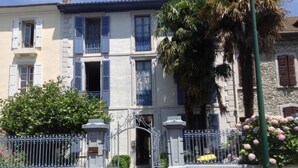 A two-story building with a gated entrance, a balcony, and a palm tree. -  BEAUTIFUL 2-ROOM APARTMENT "DESIGN" calm GROUND FLOOR LE LOGIS LE COL D'ASPIN (Lourdes)