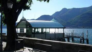 A lakeside pavilion with a glass roof, a bench, and a lamp post.